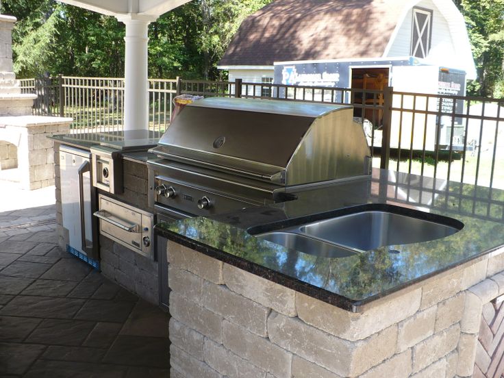 an outdoor kitchen with stainless steel appliances and granite counter tops, under a gazebo