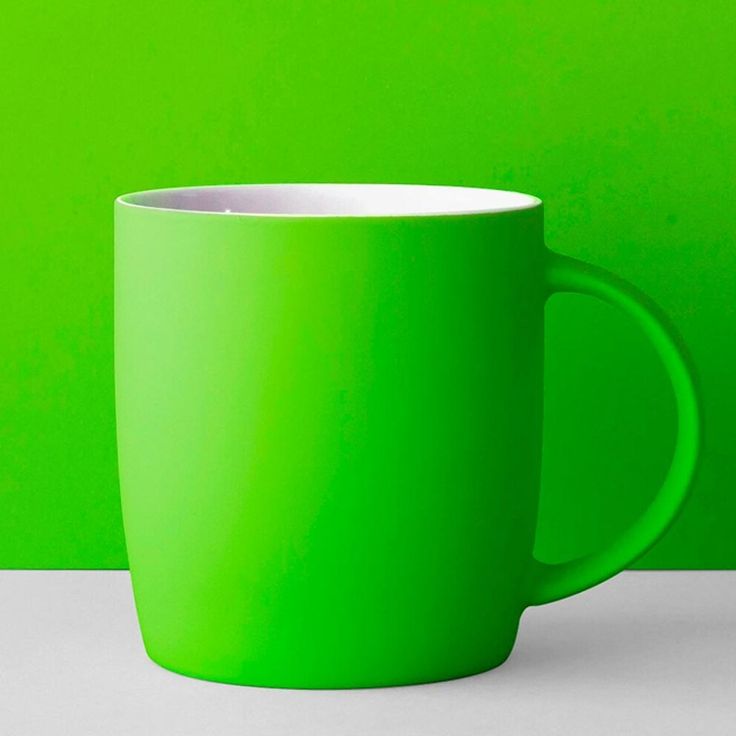 a green coffee cup sitting on top of a white table next to a green wall