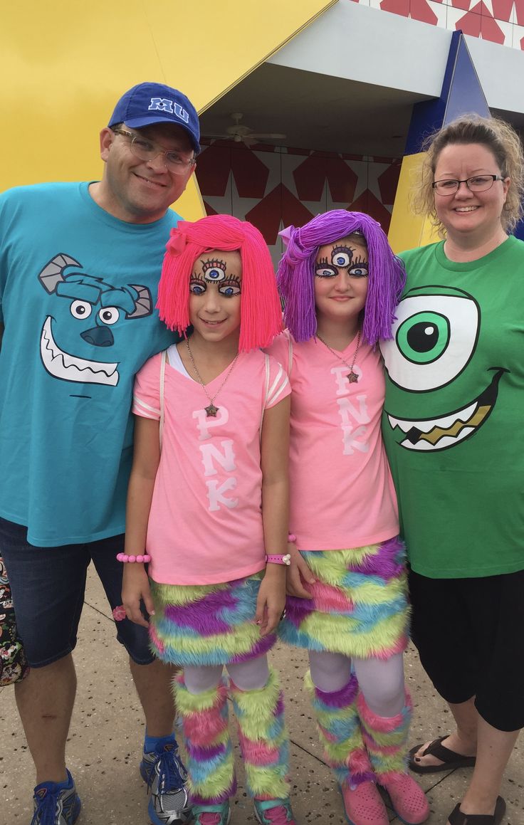 three adults and two children in costume posing for a photo at an amusement park with monster faces on their shirts