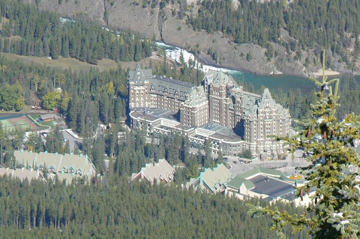 an aerial view of a large building in the middle of some trees and mountains with a body of water behind it