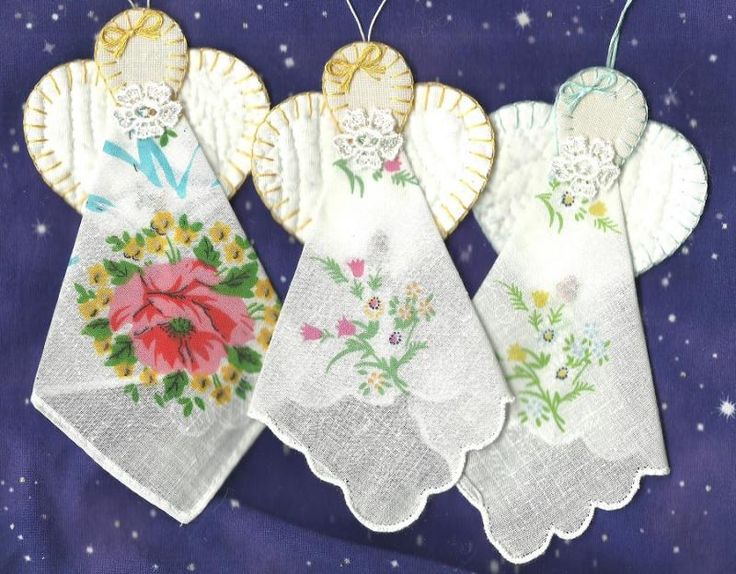 three white tea towels with floral designs hanging from strings on a purple cloth covered surface