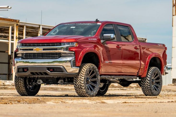 a red truck is parked in front of a building with large tires on it's rims