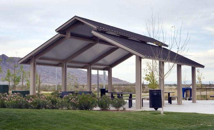 a covered picnic area in the middle of a park with mountains in the back ground