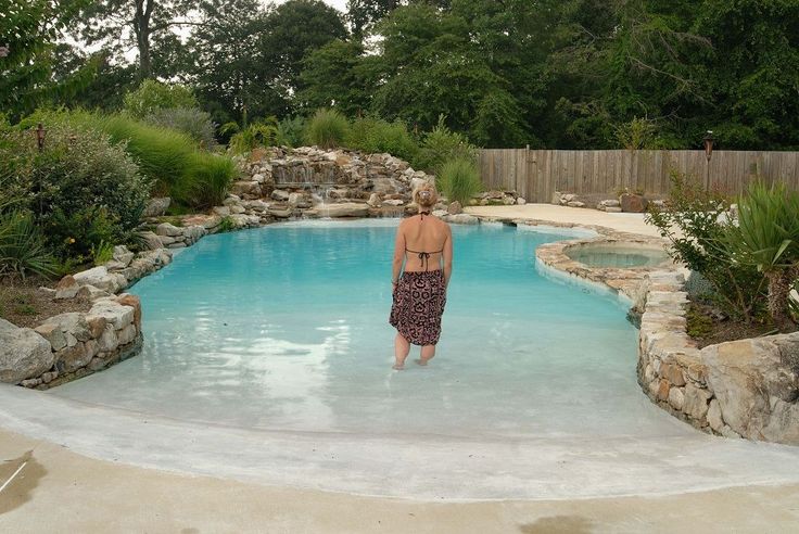 a woman standing in the middle of a pool with rocks and trees around her area