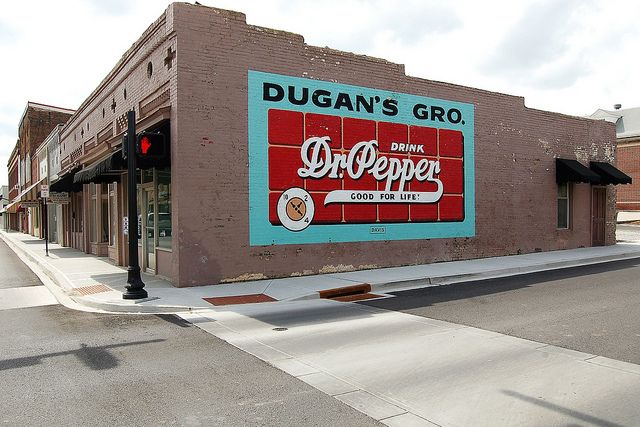 a street corner with an old dr pepper sign on the side of a building that says dugan's gro