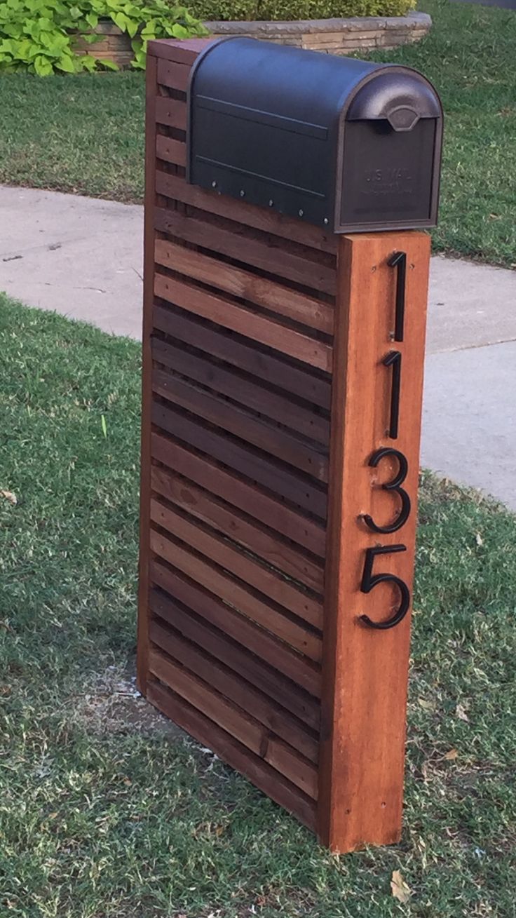 a wooden mailbox sitting in the grass next to a sidewalk