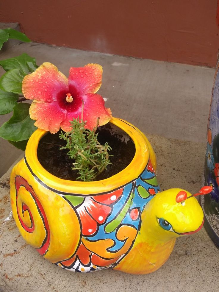 a yellow bird planter next to a flower pot with a pink flower in it