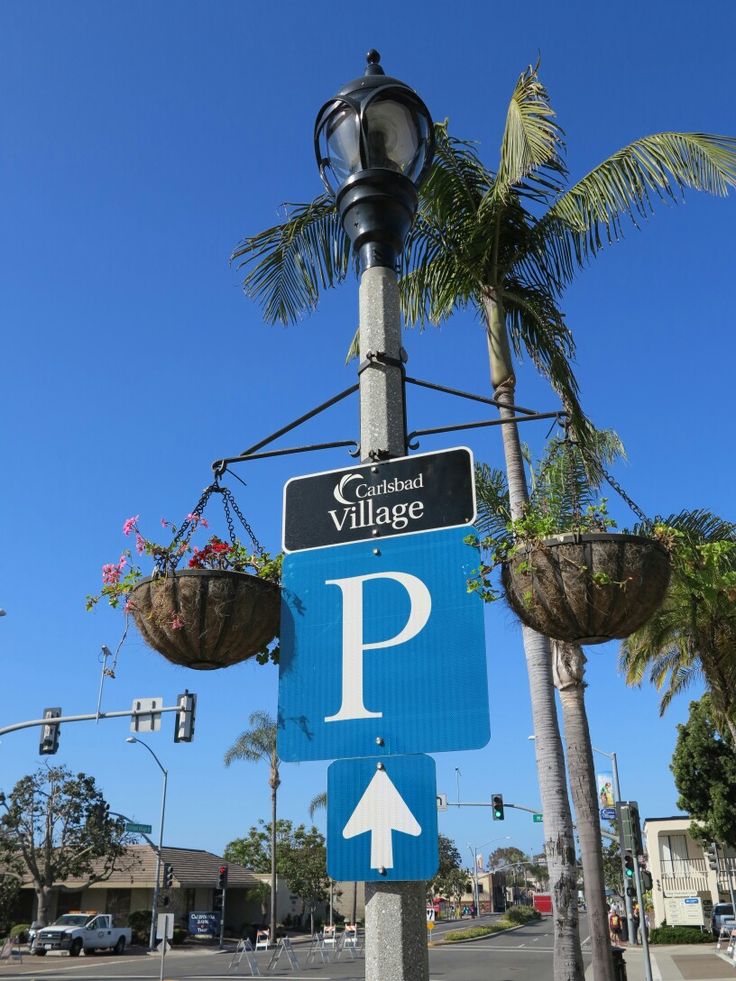 a blue street sign sitting on the side of a road next to palm trees and traffic lights