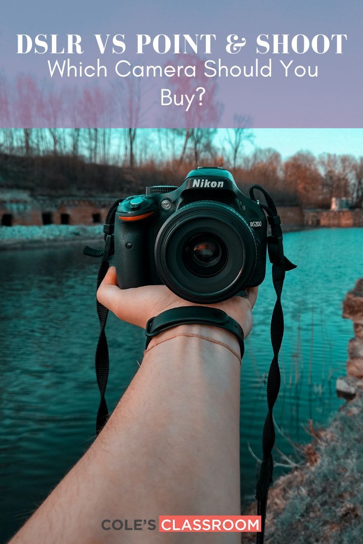 a person holding up a camera near a body of water with trees in the background