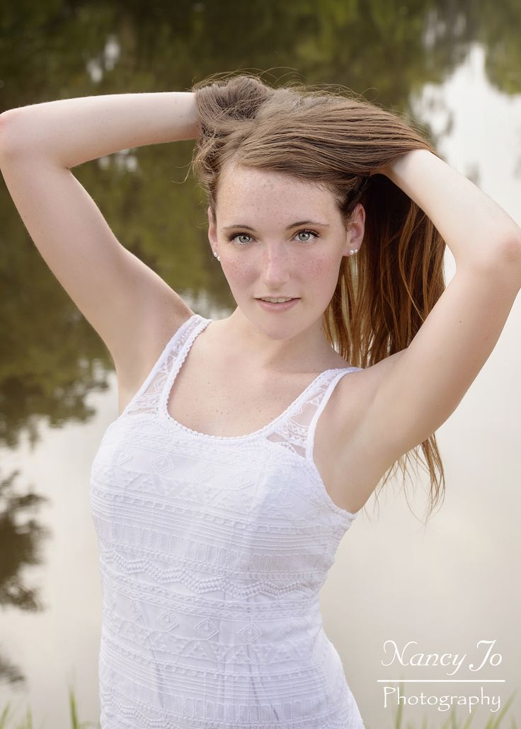 a beautiful young woman posing in front of a lake with her hair blowing in the wind