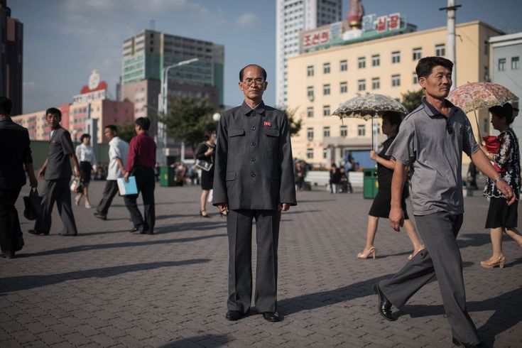 two men are walking down the street with an umbrella over their heads and people in the background