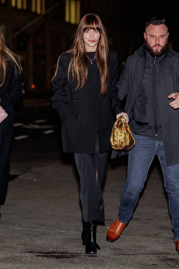 two people are walking down the street at night, one is carrying a handbag