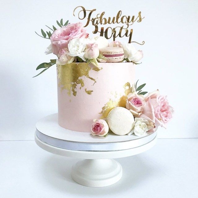 a pink and gold birthday cake with flowers on top