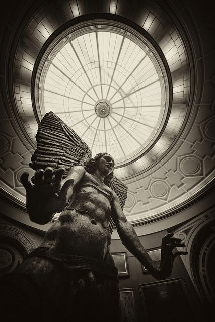 a statue in front of a round window with a skylight above it and a man holding an object up to his chest