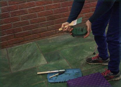 a person standing on the ground holding a green bucket and some baseball bats next to a brick wall