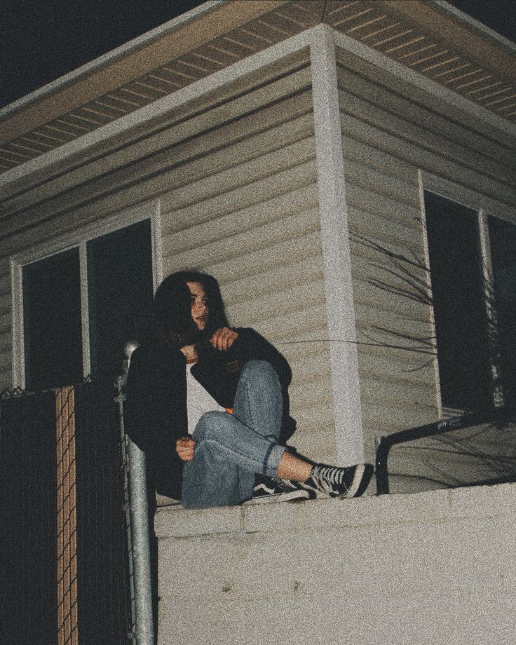 two people sitting on the ledge of a house at night with their arms around each other