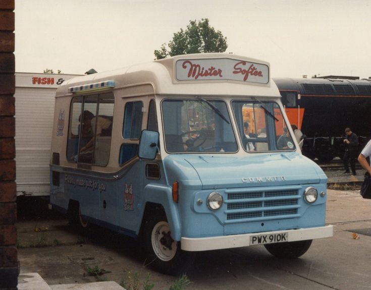 an old ice cream truck parked in front of a building with people standing around it