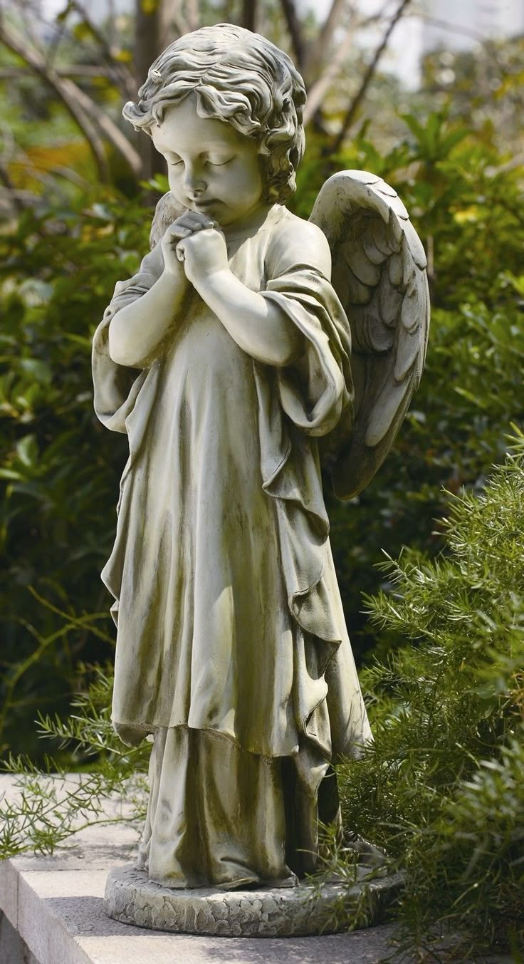 an angel statue sitting on top of a cement slab in front of trees and bushes