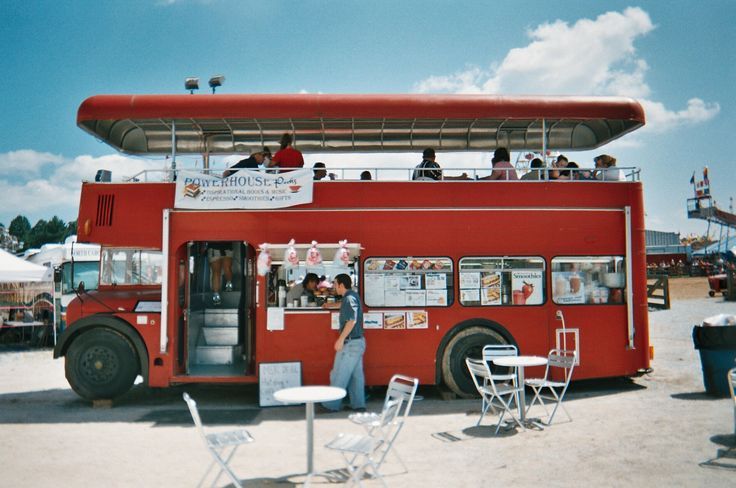 a red double decker bus with people sitting on the top and standing in front of it