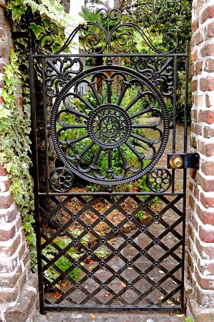 an iron gate with a circular design in the center surrounded by brick walls and plants