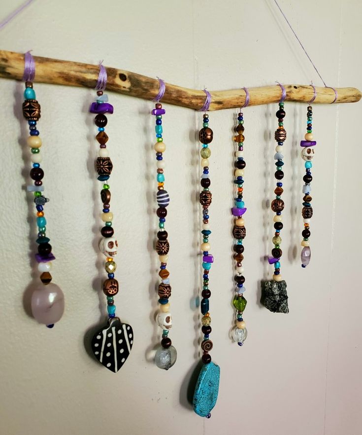 a wall hanging with beads, stones and other items on it's side next to a wooden stick