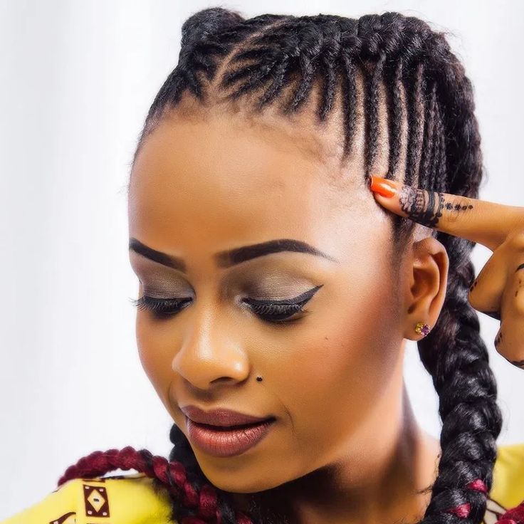 a woman with braids and makeup looks down at her hair while wearing a yellow top