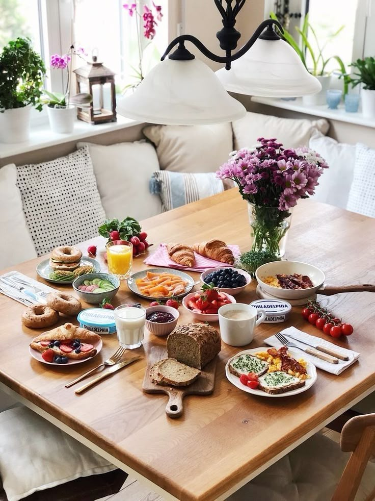 a wooden table topped with plates and bowls of food next to a vase filled with flowers