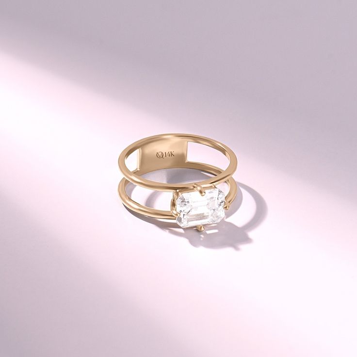 a gold ring with a white diamond in the center on a light pink background,