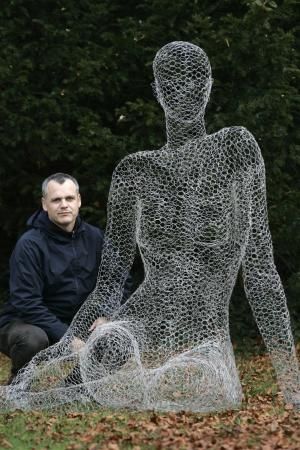 a man kneeling down next to a wire sculpture