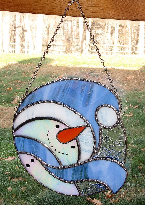 a stained glass fish hanging from a chain on the grass with trees in the background