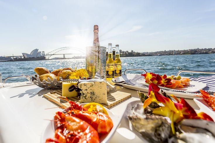 the sun shines brightly on food and drinks on a boat in the water with sydney bridge in the background