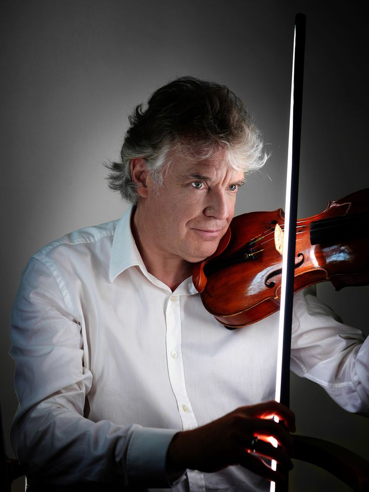 a man holding a violin in his right hand and looking at the camera with an intense look on his face