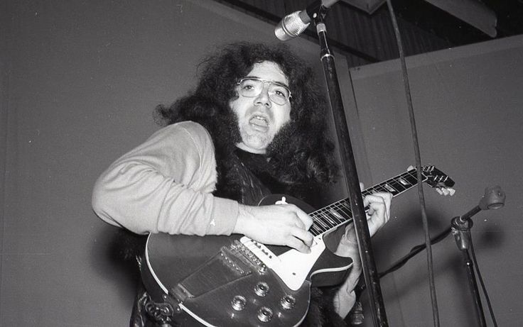 a man with long hair playing an electric guitar in front of a microphone and keyboard