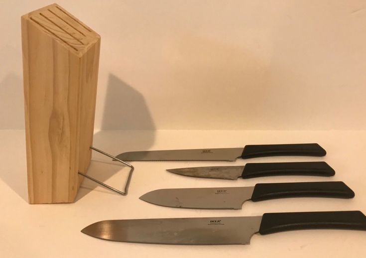 five knives are lined up next to a wooden block and knife sharpener on a white surface