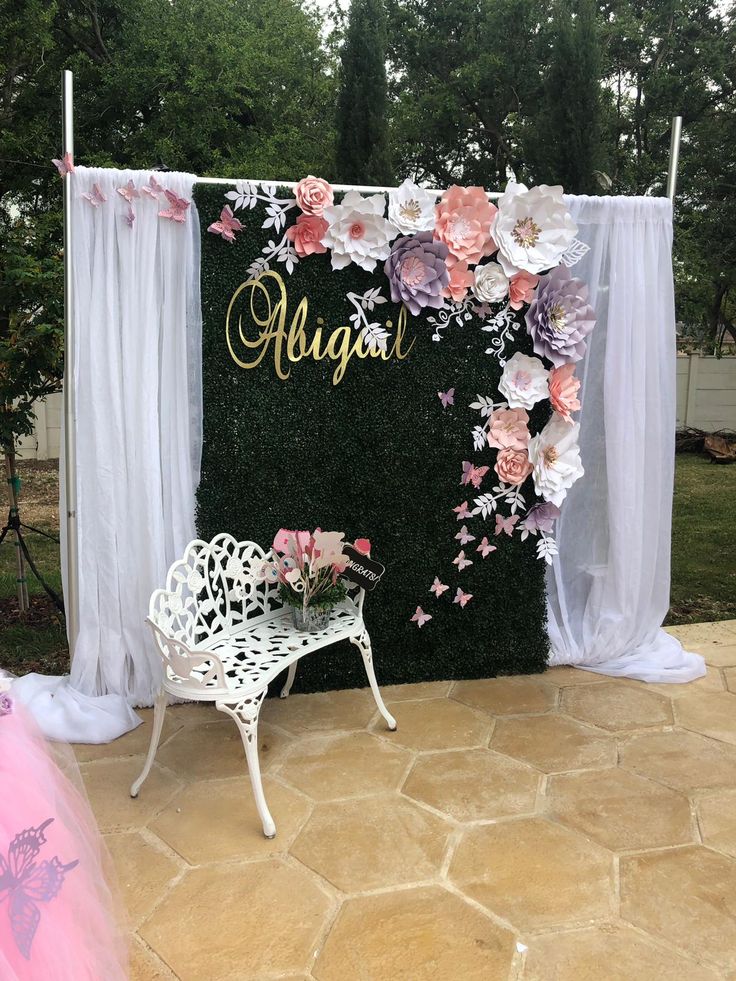 a white bench sitting in front of a flower covered wall with the word august on it