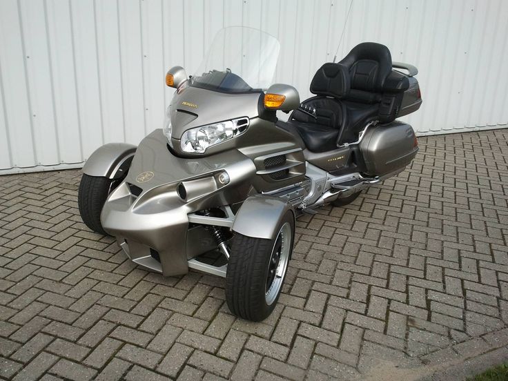 a silver motorcycle parked on top of a brick road next to a white building with a black leather seat