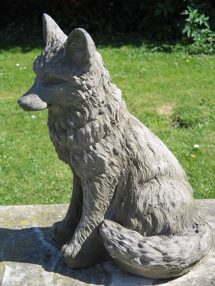 a statue of a fox sitting on top of a stone slab in front of some grass