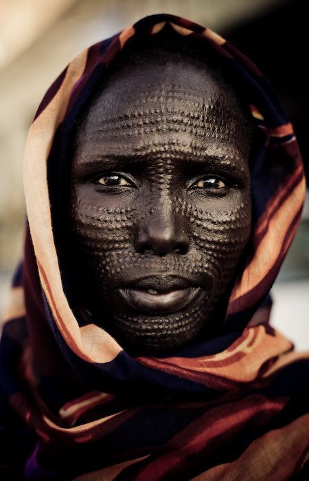 a woman with black face paint on her face and scarf around her head, looking at the camera