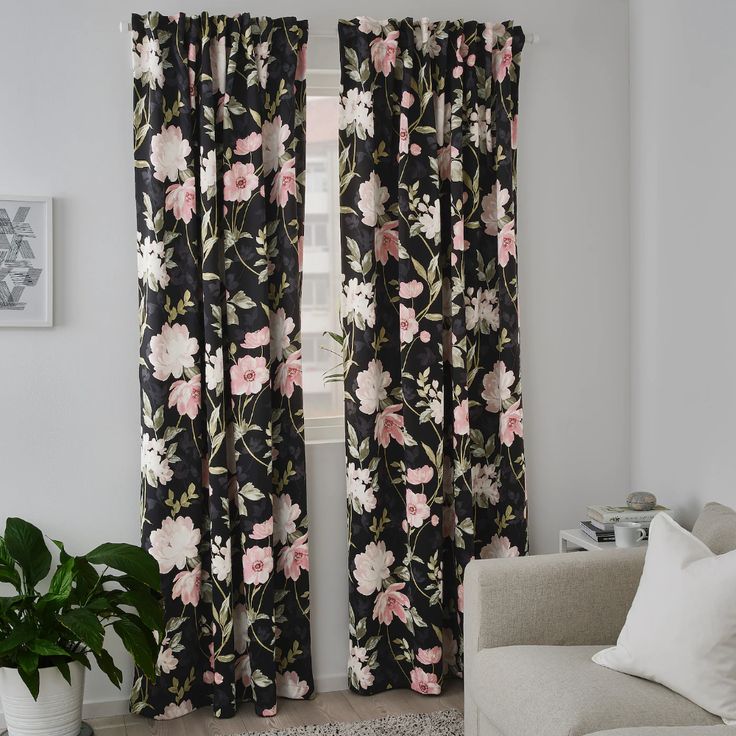 a living room filled with furniture and a window covered in black floral print curtains next to a white couch