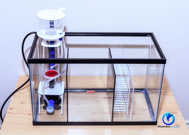 a clear box with some tools inside on a wooden table next to a white wall