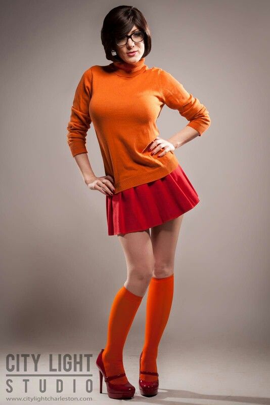 a woman in an orange sweater and red skirt posing for the camera with her hands on her hips