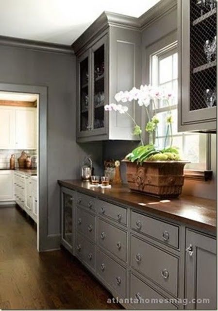 a kitchen with gray cabinets and wood flooring is pictured in this image, there are flowers on the counter