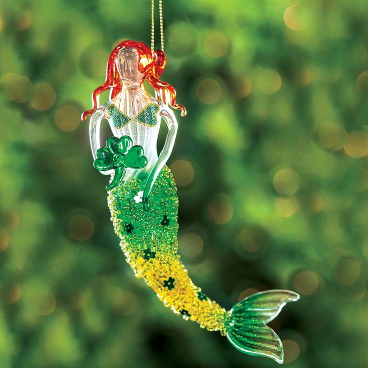 a glass ornament shaped like a mermaid with green and yellow flakes hanging from it's side