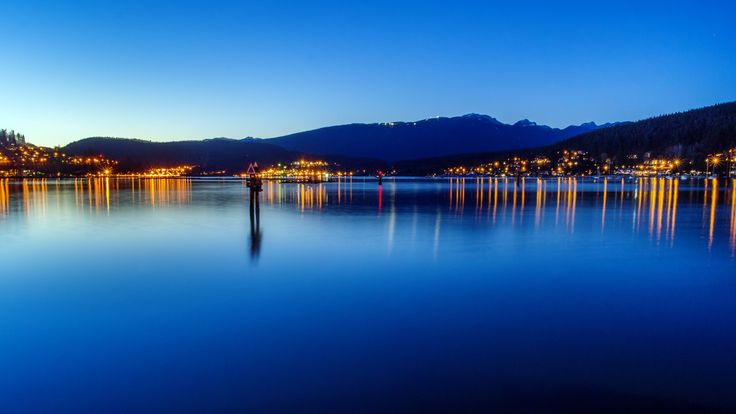 a body of water that has some lights on it and mountains in the back ground