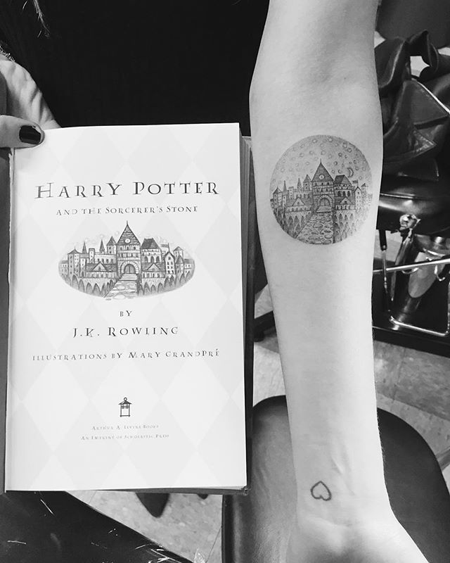 a person with a tattoo on their arm holding a harry potter book in front of them