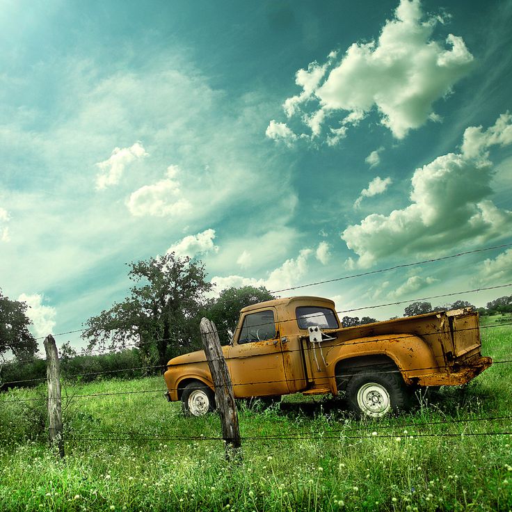 an orange truck parked on top of a lush green field next to a wooden fence