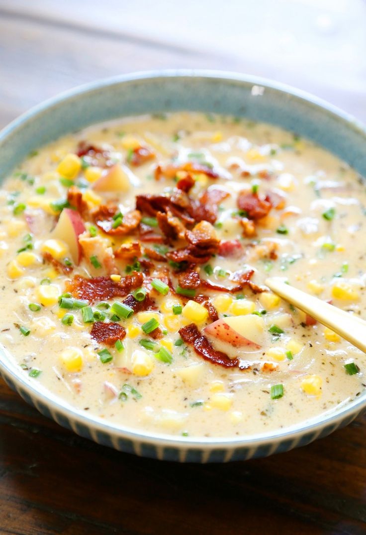 a bowl of soup with bacon, corn and cheese in it on a wooden table