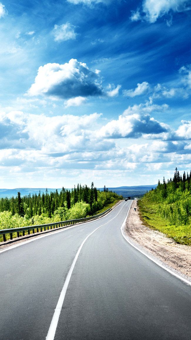 an empty road with trees on both sides and blue skies above it in the background