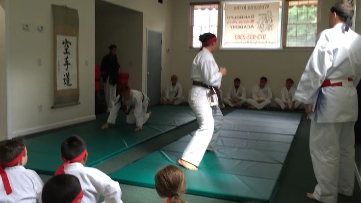 some people are doing karate in a room with green mats on the floor and one person is standing up