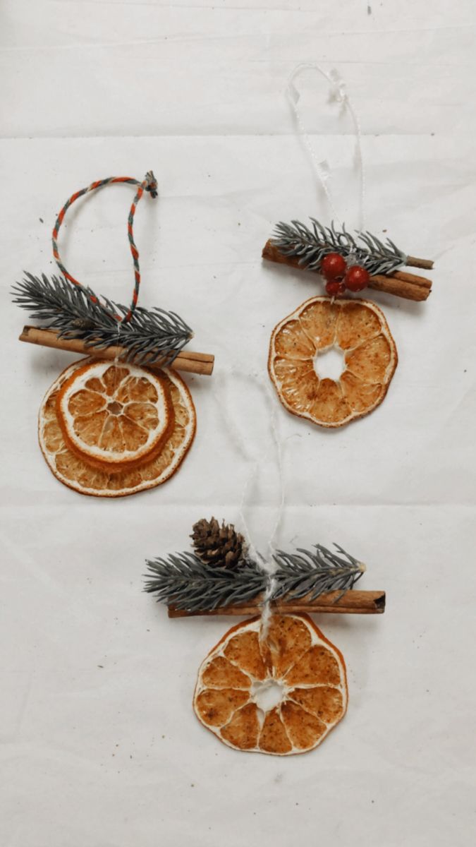 three orange slices and cinnamon sticks are hanging from twine on a white tablecloth